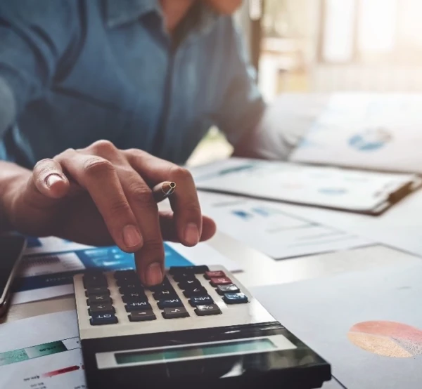 Guy using calculator on a desk while looking at charts