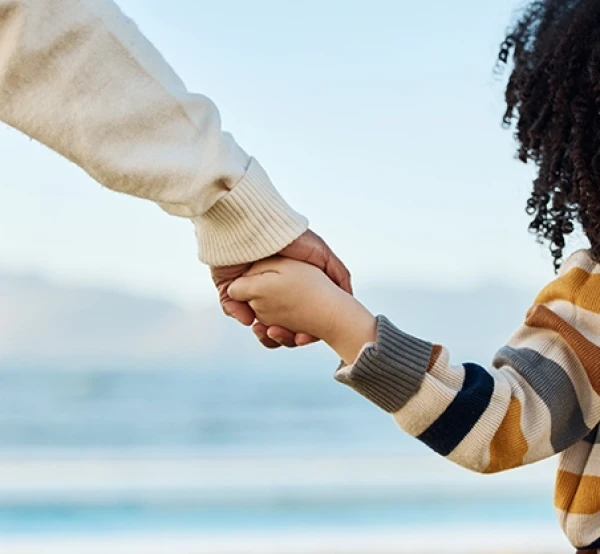 Small boy holding adult's hand while looking out to sea