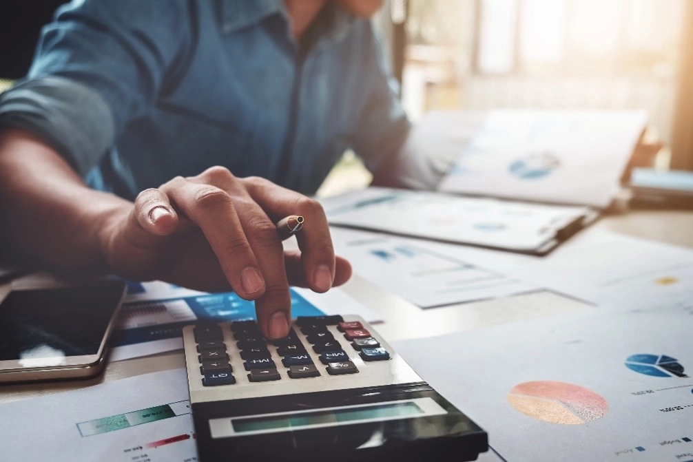 Guy using calculator on a desk while looking at charts